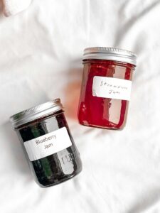 Two jars of homemade blueberry and strawberry jam on a white surface.